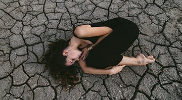 Frau mit Scheidentrockenheit krümmt sich auf einem trockenen Boden